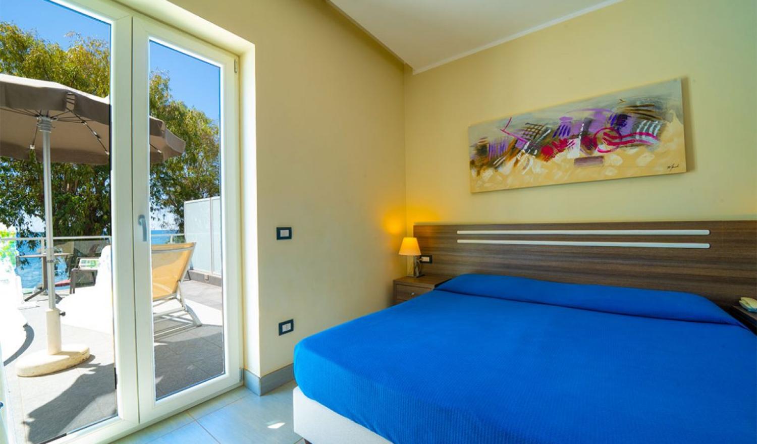 Camera moderna con letto blu e terrazza vista mare.