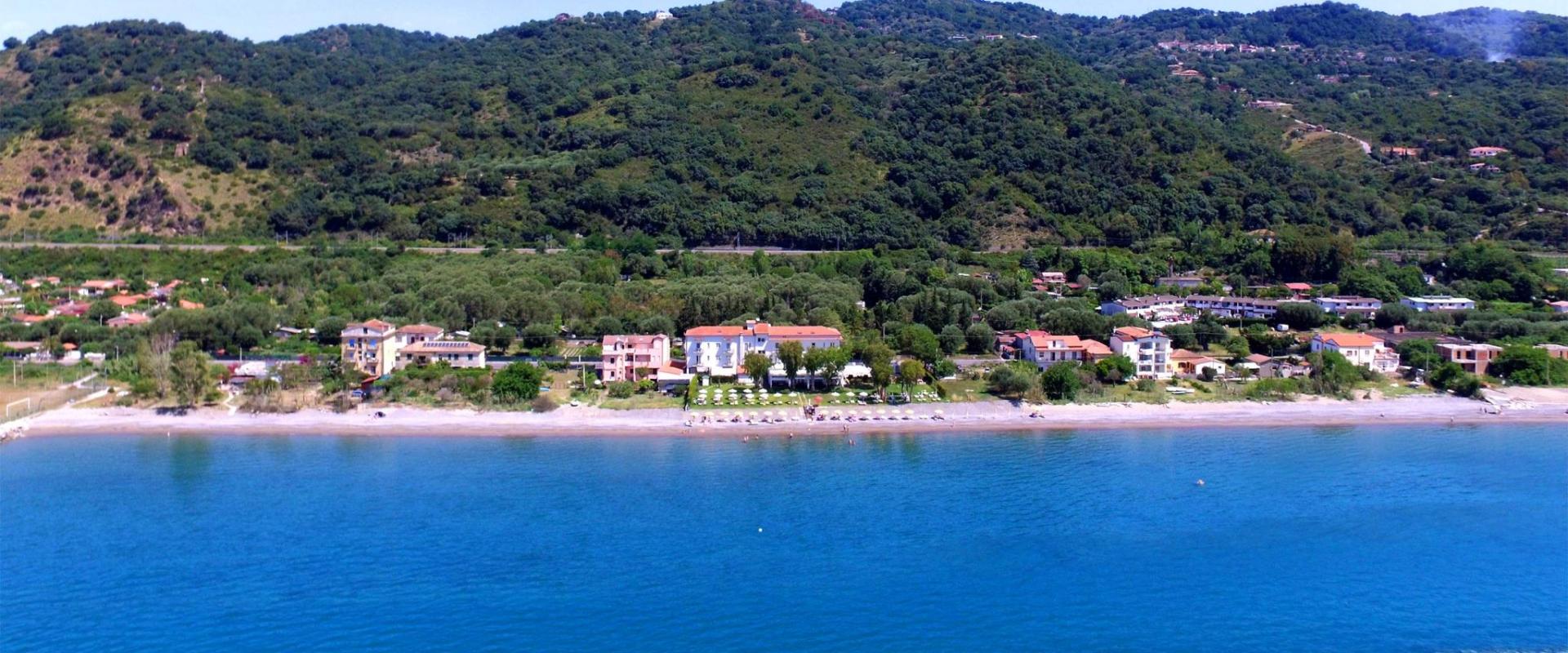 Spiaggia con mare cristallino e colline verdi sullo sfondo.
