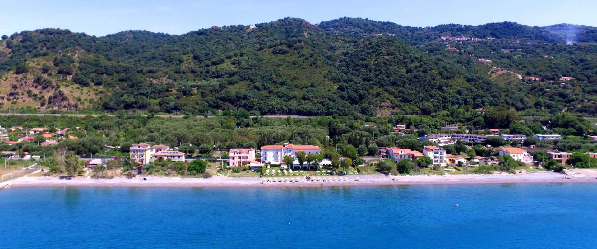Spiaggia con mare cristallino, alberi verdi e colline sullo sfondo.
