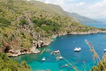 Baia con acque turchesi e barche, circondata da colline verdi e rocce.