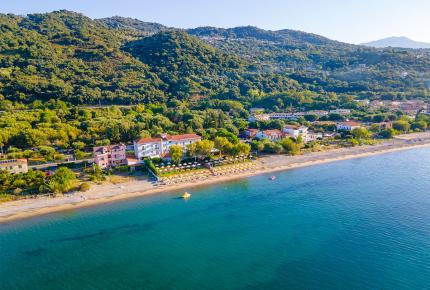 Spiaggia tranquilla con ombrelloni, mare cristallino e colline verdi sullo sfondo.