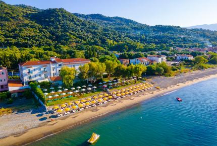 Beach with yellow umbrellas, hotel, and green hills in the background.