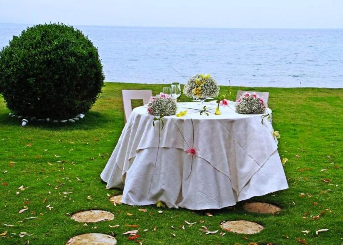 Tavolo all'aperto decorato con fiori, vista mare, atmosfera romantica.
