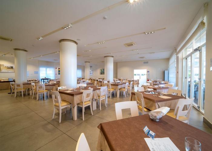 Ristorante spazioso con tavoli apparecchiati e ampie finestre luminose.
