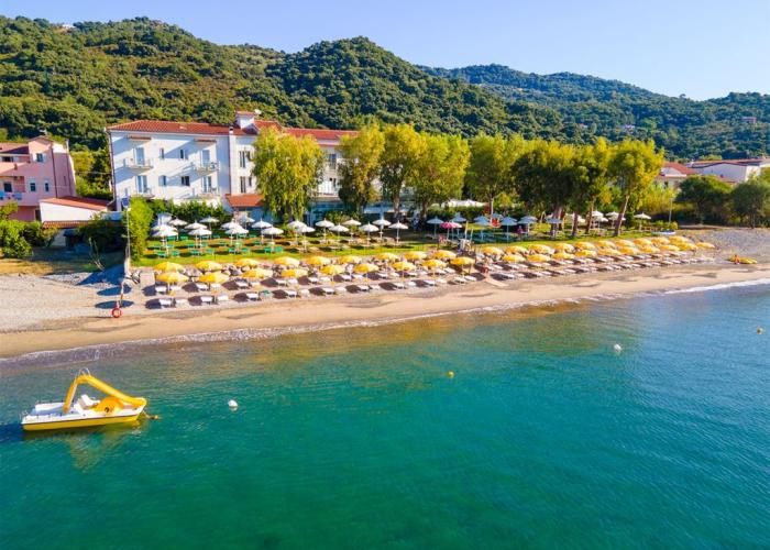 Spiaggia con ombrelloni gialli, hotel e pedalò, circondata da colline verdi.