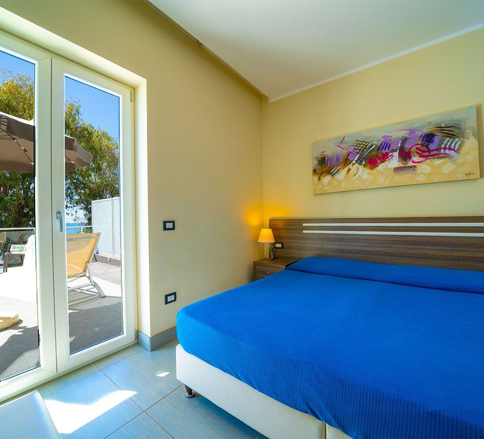 Camera luminosa con letto matrimoniale, arte moderna e accesso al terrazzo.