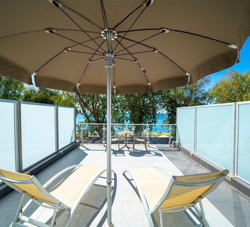 Terrazza con lettini, ombrellone e vista mare, ambiente rilassante e soleggiato.