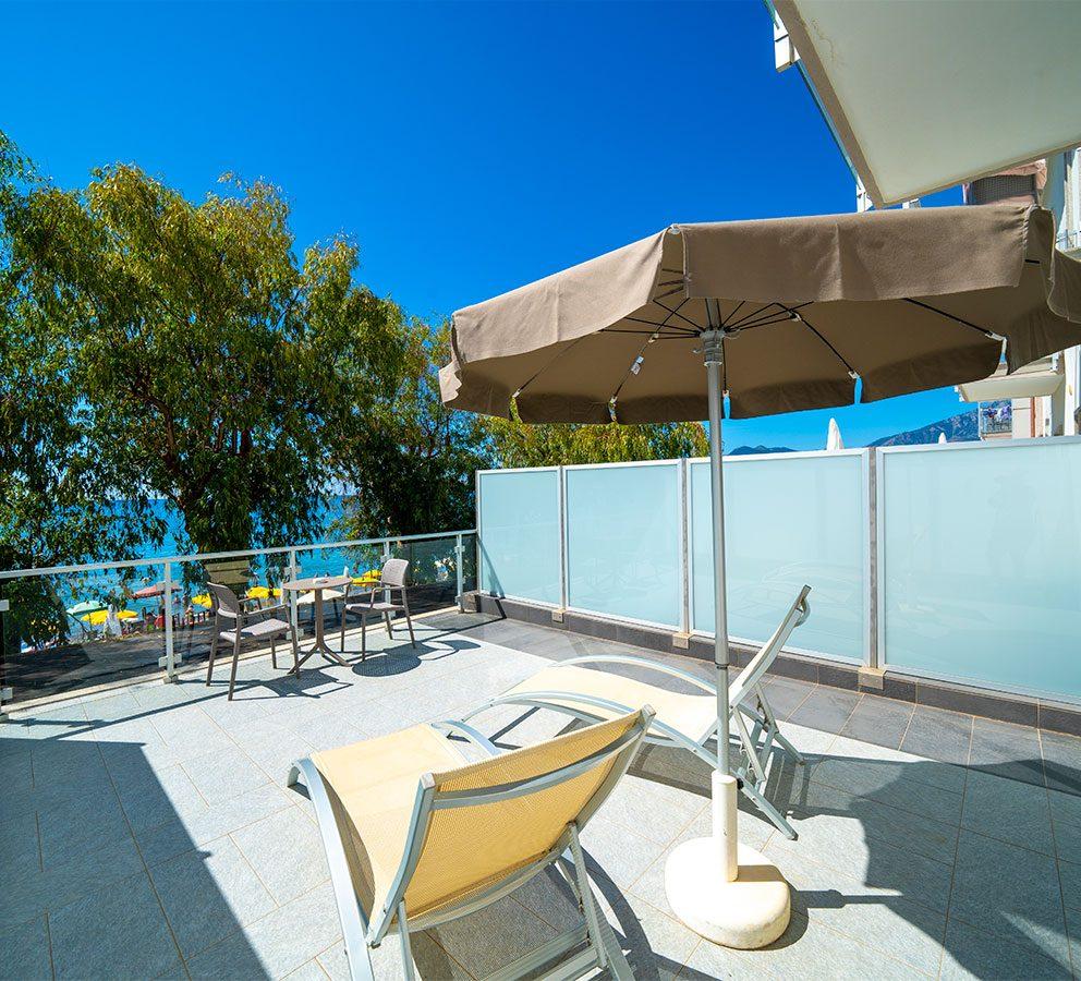 Terrazza soleggiata con sedie a sdraio e ombrellone, vista mare.