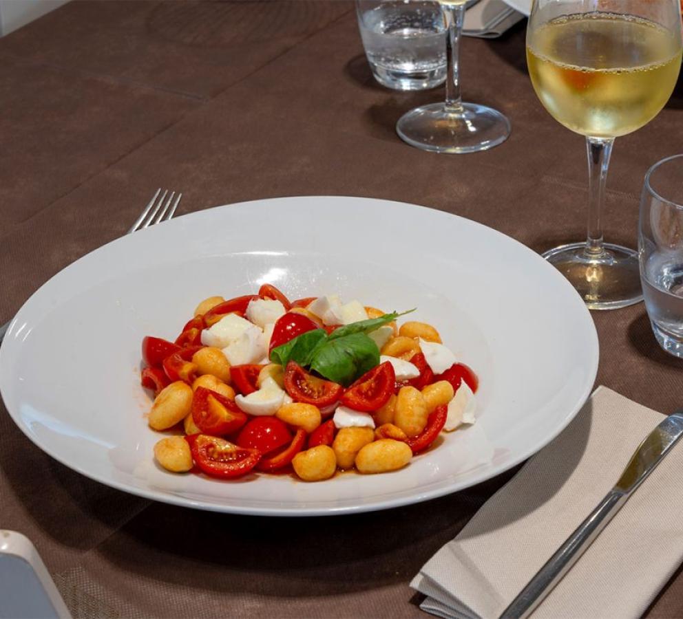 Gnocchi con pomodorini, mozzarella e basilico, accompagnati da un bicchiere di vino bianco.