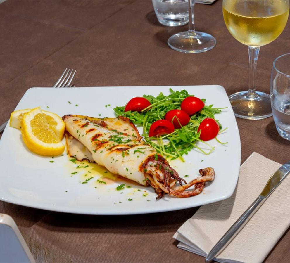 Calamari alla griglia con rucola, pomodorini e limone, accompagnati da vino bianco.